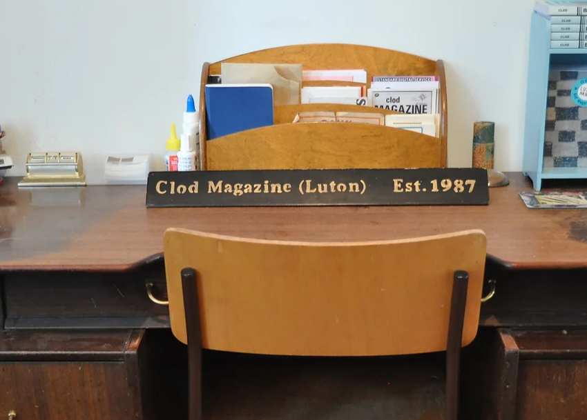 Desk with writing materials and sign with Clod Magazine written on it.